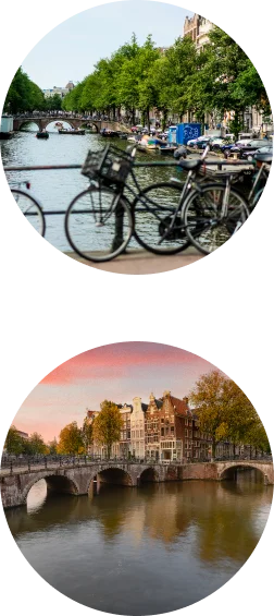 Klassiek Amsterdams stadsbeeld met fietsen, grachtenbruggen, boten en met bomen omzoomde straten tijdens de dag.